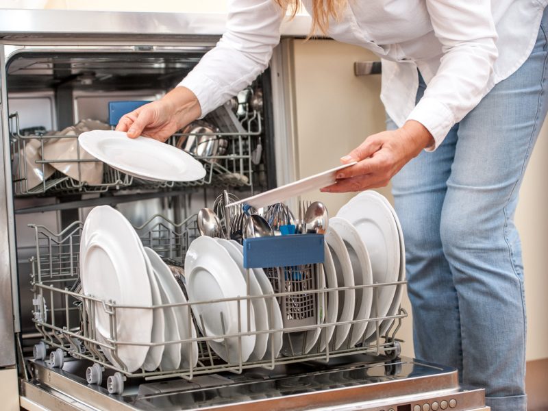Adult Woman Unloading Dishwasher In The Kitchen
